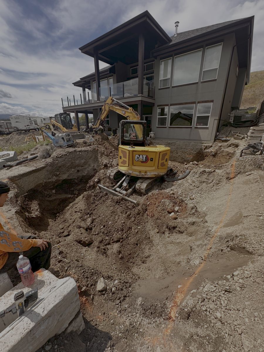 Excavator digging a pool beside a new home